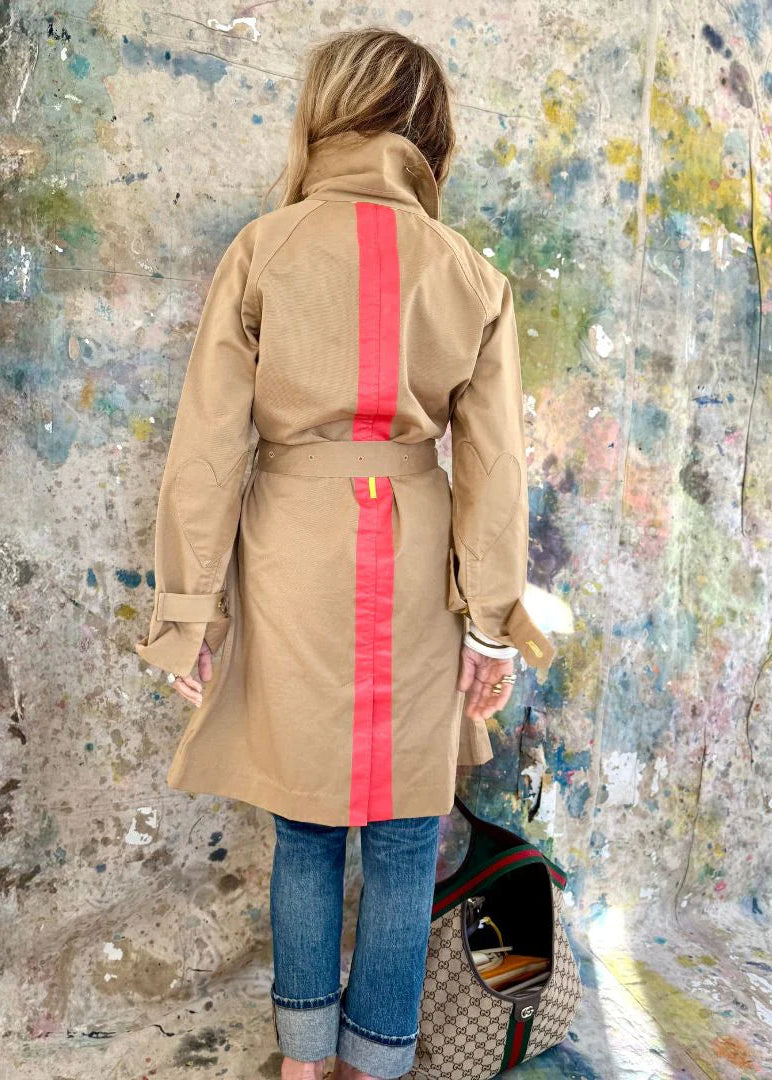 Person wearing a beige trench coat with red stripes against a textured wall.