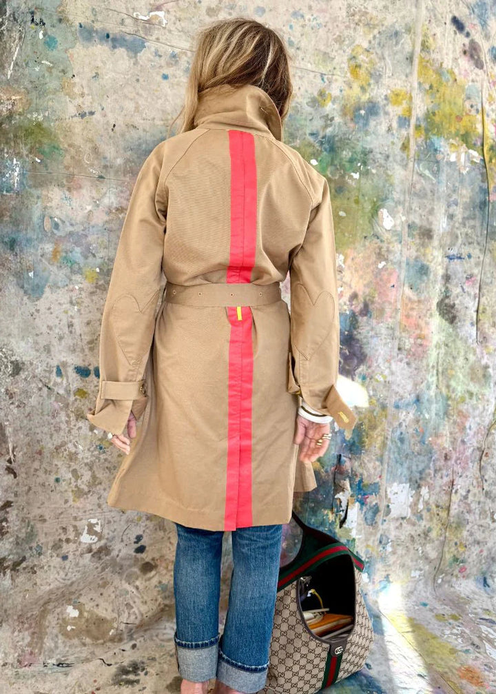 Person wearing a beige trench coat with red stripes against a textured wall.